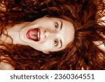 Small photo of Overhead shot of a spirited young woman with wide-open mouth showcasing flawless teeth. Her vibrant eyes and red lipstick juxtapose against her long red hair, exuding joy and magnetism