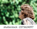 Small photo of With sun-drenched woods in the background, an aged woman looks skyward. Her chunky glasses are noticeable, and her sparse hair reveals a '50s perm and gray roots, echoing Marilyn Monroe's era