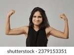 Small photo of With a straightforward background, a woman stands firm, arms flexed. Their attire, a simple black sleeveless top, is in harmony with their confident demeanor and tousled hair