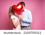 Couple kissing hidden behind one heart shape balloon