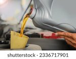Small photo of Change the engine oil as scheduled. A clear golden oil like topaz flows from a plastic gallon into the engine of a private car.