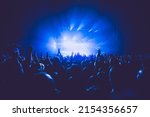 A crowded concert hall with scene stage lights in blue tones, rock show performance, with people silhouette, on a dance floor air during a concert festival