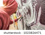 Street artist painting colorful graffiti on public wall - Modern art concept with urban guy performing and preparing live murales with multi color aerosol spray - Sunshine filter with focus on monster