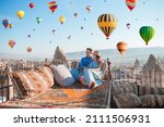 Young couple at sunrise on a rooftop in Cappadocia with hot air balloons in the background. Couple travels the world. Hot air balloon flights.