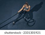 Power sporty female athlete exercising with rope at a gym top view.