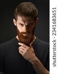 Small photo of Serious brutal bearded man on dark background. Young bearded man combing his beard.
