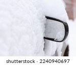 Only side mirror of car is visible from under the snow. A parked passenger car was covered with snow in an open parking lot due to heavy snowfall
