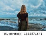 A young woman is standing by the sea watching the waves break