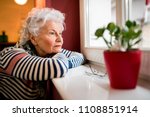 Sad alone senior woman looking through window at home, loneliness concept