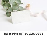 Bright feminine spring stationery mockup scene with a handmade paper greeting card, spool of silk ribbon and eucalyptus leaves on a white table background. Wedding styled stock photography.