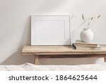 Horizontal white frame mockup on vintage wooden bench, table. Modern white ceramic vase with dry Lagurus ovatus grass and books. White wall background. Scandinavian interior. Selective focus.