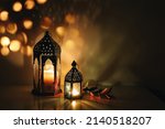Decorative Arabic lanterns with burning candles at night. Glittering golden bokeh lights. Festive greeting card, invitation. Muslim holy month Ramadan Kareem, dark background with olive branch.