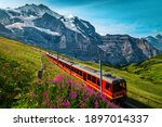 Cogwheel railway with electric red tourist train. Snowy Jungfrau mountains with glaciers, flowery fields and red passenger train, Kleine Scheidegg, Grindelwald, Bernese Oberland, Switzerland, Europe