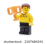 Small photo of Lorrach, Germany - 011622: Lego minifigure in uniform holds a golden cup or prize in a hand isolated on white. Editorial illustrative image of reward ceremony and results.
