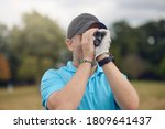 Golfer using a rangefinder to measure the distance to the hole holding it to his eye as he peers down the fairway in a close up head and shoulders for a healthy active lifestyle or sport concept