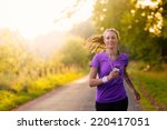 Woman listening to music on her earplugs and MP3 player while jogging along a country road in a healthy lifestyle, exercise and fitness concept