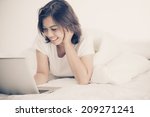 Smiling woman using a laptop while lying on her bed