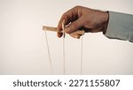 Small photo of The hand of a man in a gray shirt controls a puppet using a wooden manipulator and strings. Hand handling at puppet by pulling strings to make the character move. White background. Close up.