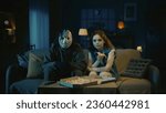 Small photo of Man horror maniac and young girl sitting on the sofa in the room, girl eats pizza, both looking at the camera.