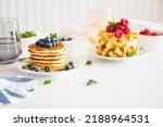 Summer breakfast. Homemade baked ricotta pancakes and Belgian waffles with fresh berries on white wooden table, copy space