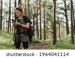 Young female hiker is using smartphone for navigation in green forest