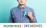 Small photo of Asian portrait happy handsome man posing he holding light blue ribbon for supporting people living and illness, studio shot isolated on blue background, Prostate Cancer Awareness concept