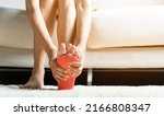 Small photo of Foot pain, Asian woman sitting on sofa feeling pain in her foot at home, female suffering from feet ache use hand massage relax muscle from soles in home interior, Healthcare and podiatry medical