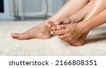 Small photo of Foot pain, Asian woman holds her toe injury feeling pain her foot at home, female suffering from feet ache use hand massage relax muscle from toe in house interior, Healthcare problems medical concept