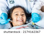 Small photo of Dental kid health examination. Doctor examines oral cavity of little child uses mouth mirror to checking teeth cavity, Asian dentist making examination procedure for smiling cute little girl