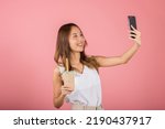Asian woman takes photo of herself with drinking brown sugar flavored tapioca pearl bubble milk tea, smile female making selfie, studio isolated on pink background, pearl milk tea beverage concept