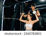 Small photo of Asian fitness instructor teaching a smiling woman proper lifting techniques, using weight lifting equipment for a safe and effective workout, technique of exercise in gym dark gym background