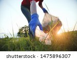 volunteer young woman collecting garbage, picking up waste at sunset light, land pollution, environmental problem