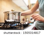 Beautiful young woman housewife prepairing dinner, hold in hands big steel saucepan, standing it on gas-stove.