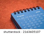Small photo of August 2022 - spiral desktop calendar against red mulberry paper, time and business concept