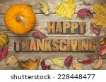 Happy Thanksgiving  - text in vintage letterpress wood type blocks against rustic wood background with a pumpkin and dry leaves