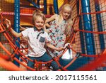 Happy group of siblings playing together on indoor playground. Excited kids playing together on net ropes. Cute school kids playing on the colorful playground at shopping mall
