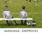 Small photo of Two School Boys in Sports Football Team. Kids in Classic Soccer Jersey Uniforms With Numbers. Kids Playing Sports Together. Children Resting and Sitting on Sideline Substitute Bench