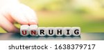 Small photo of Hand turns dice and changes the German word "unruhig" ("twitchy") to "ruhig" ("calm").