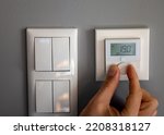 Hand turns down the temperature to 19 degrees Celsius on a electronic thermostat. Symbol for saving energy.