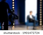 Cameraman filming in tv talk show studio. The host or presenter sitting on a chair camera pointed at him. Television news live broadcast production set