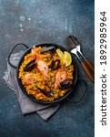 Small photo of Classic dish of Spain, seafood paella in traditional pan on rustic blue concrete background top view. Spanish paella with shrimps, clamps, mussels, green peas and fresh lemon wedges from above
