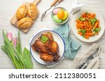 Easter food on white rustic table: pastel colored eggs, roasted chicken and vegetables, buns and spring flowers tulips top view flay lay, Easter family dinner meal with festive dishes 