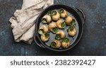 Small photo of Escargots de Bourgogne Cooked Snails with Garlic Butter and Parsley in black cast iron pan on rustic stone background from above, traditional French Delicacy .