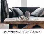 Minimalistic home decor on rustic coffee table over black sofa with cushions. Grey vases and spring flowers on wooden bench in small dark room interior. Scandinavian home style.