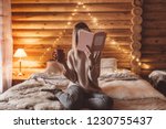 Woman relaxing and reading book on cozy bed in log cabin in winter
