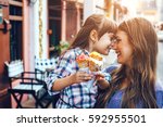 Mom with her 6 years old daughter walking along city street and eating ice cream in front of the outdoor cafe. Good relations of parent and child. Happy moments together.