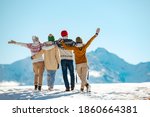 Small photo of Four happy friends are standing and embracing against snow capped mountains at sunny day. Winter vacations concept