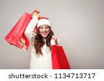 Young woman in santa hat with shopping bags on grey background