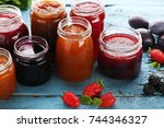 Glass jars with different kinds of jam and berries on wooden table