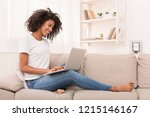 African-american woman working on laptop computer, sitting on sofa at home, copy space
